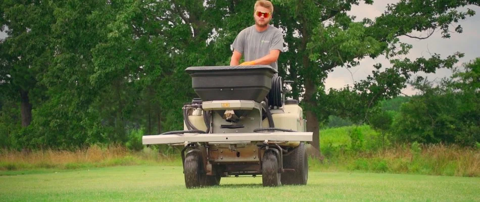 Tech treating a lawn in Charlotte, NC, with granular spreader equipment.