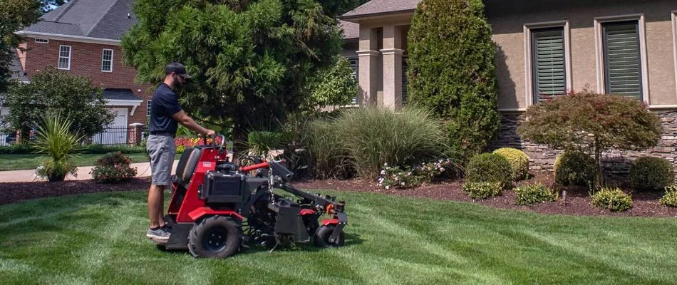 Worker aerating a lawn in Waxhaw, NC, with trees and shrubs.