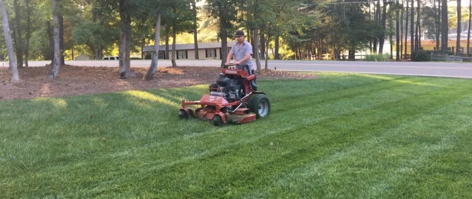 Worker riding on a mower across a lawn in Allen, NC.
